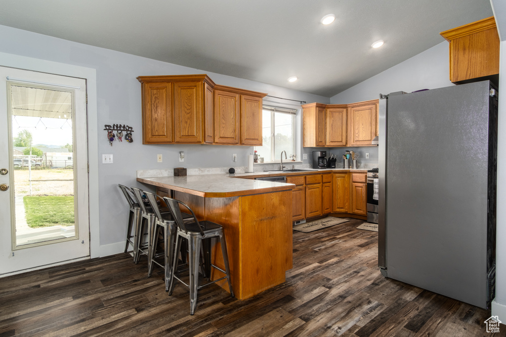 Kitchen featuring freestanding refrigerator, a sink, a peninsula, vaulted ceiling, and dark wood finished floors