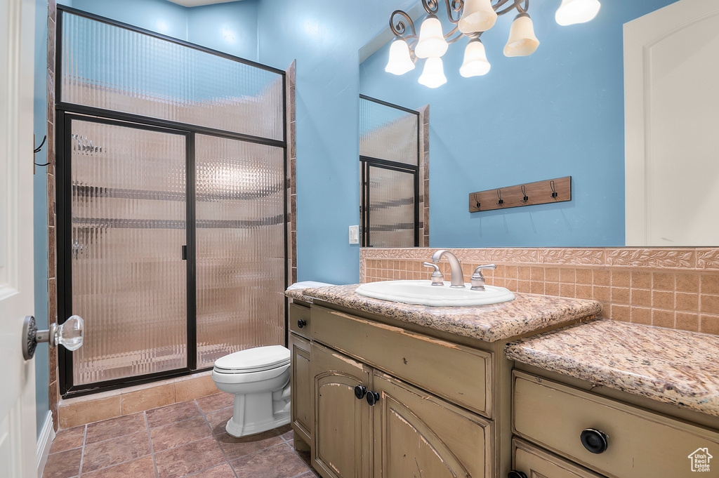 Bathroom with a shower stall, vanity, toilet, a chandelier, and stone finish floors