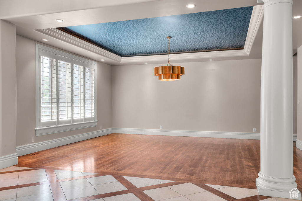 Unfurnished dining area with decorative columns, a raised ceiling, inlaid floor details, baseboards, and ornamental molding