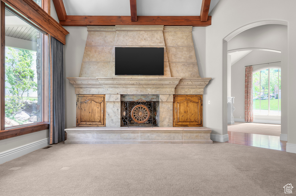 Unfurnished living room with carpet floors, baseboards, arched walkways, and beam ceiling