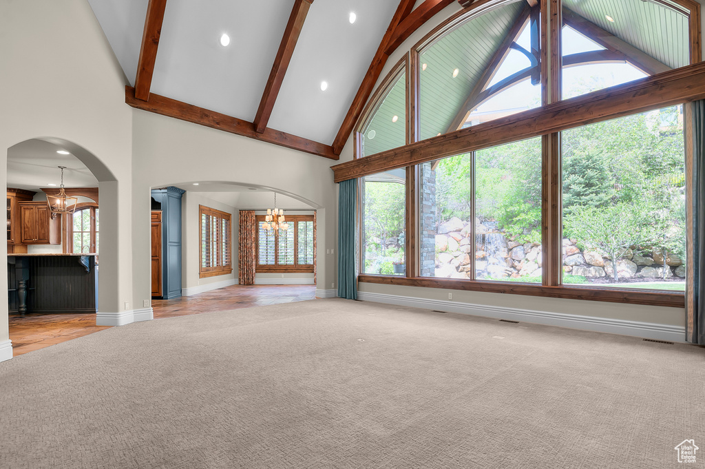 Unfurnished living room featuring a chandelier, high vaulted ceiling, ornate columns, light colored carpet, and baseboards