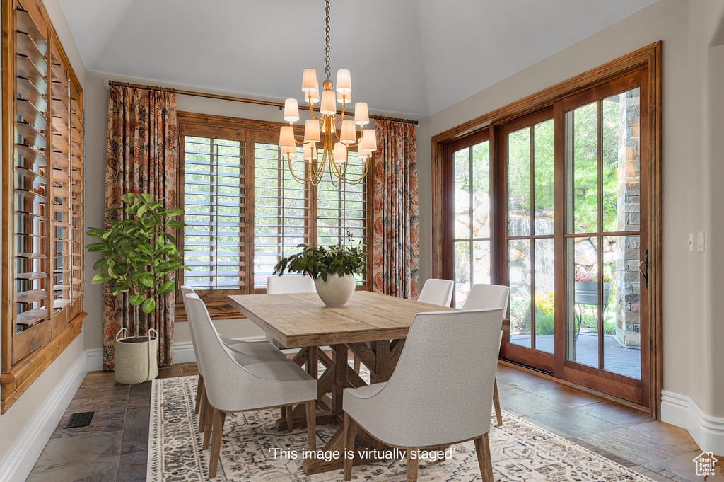 Dining area with a chandelier, lofted ceiling, healthy amount of natural light, baseboards, and stone tile flooring