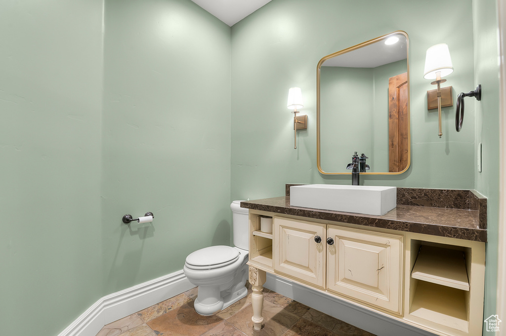 Bathroom featuring toilet, baseboards, vanity, and stone finish flooring