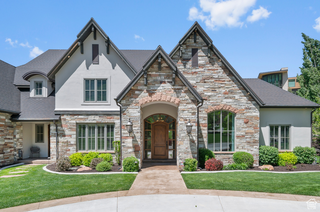 French country inspired facade with stucco siding, stone siding, and a front lawn