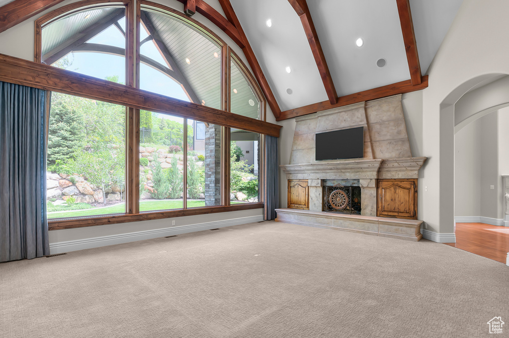 Unfurnished living room featuring carpet floors, a high end fireplace, high vaulted ceiling, beamed ceiling, and baseboards
