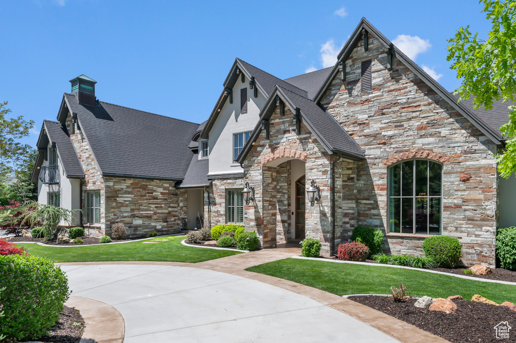 View of front facade featuring stone siding, a front lawn, a chimney, stucco siding, and a shingled roof