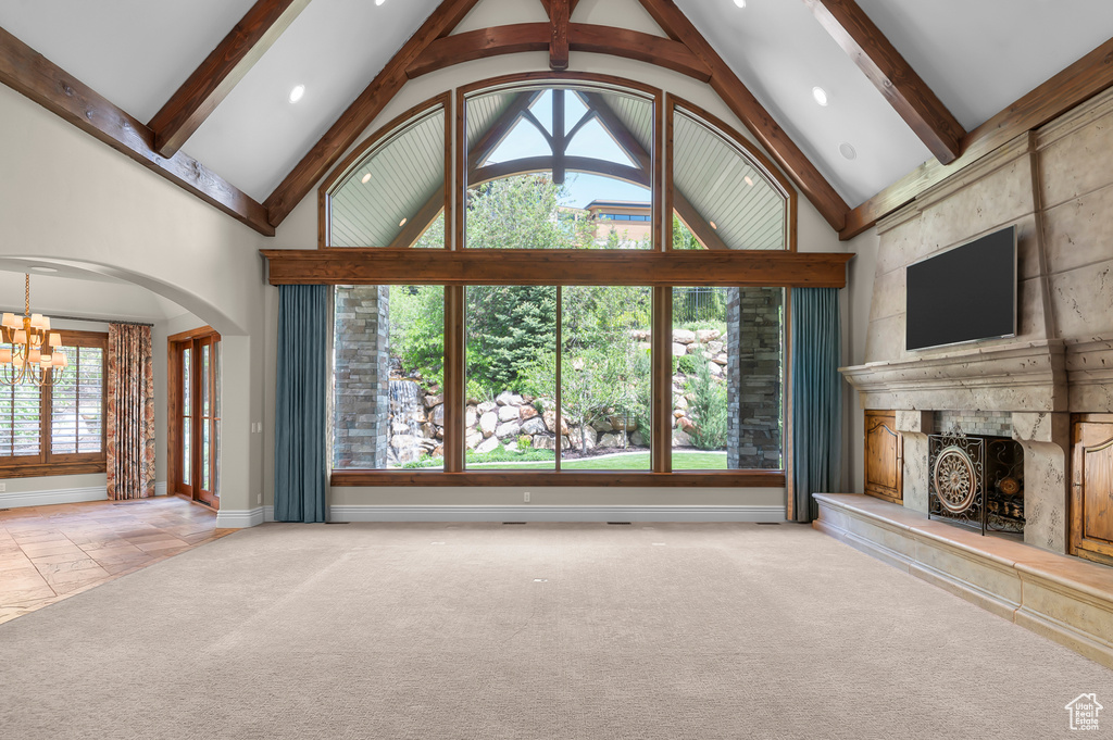 Unfurnished living room featuring a chandelier, a premium fireplace, plenty of natural light, baseboards, and beamed ceiling