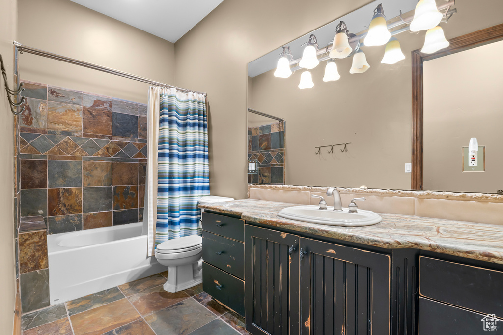 Full bathroom with vanity, toilet, shower / bath combo, and stone finish flooring