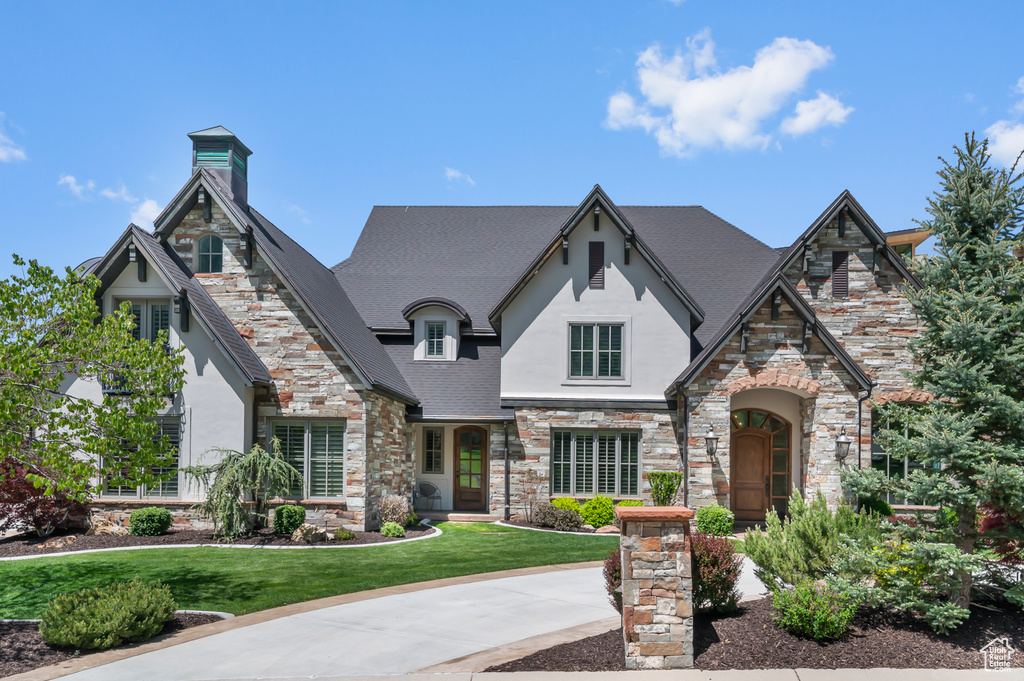 View of front of property with stone siding, stucco siding, a front yard, and a chimney