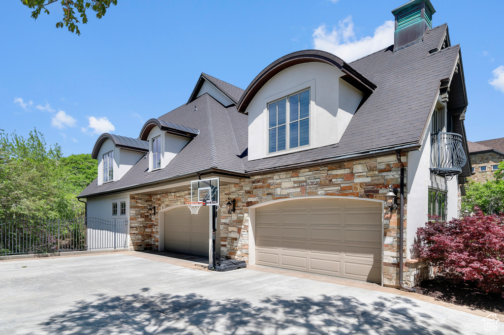 View of front of house with stone siding, concrete driveway, stucco siding, fence, and a garage