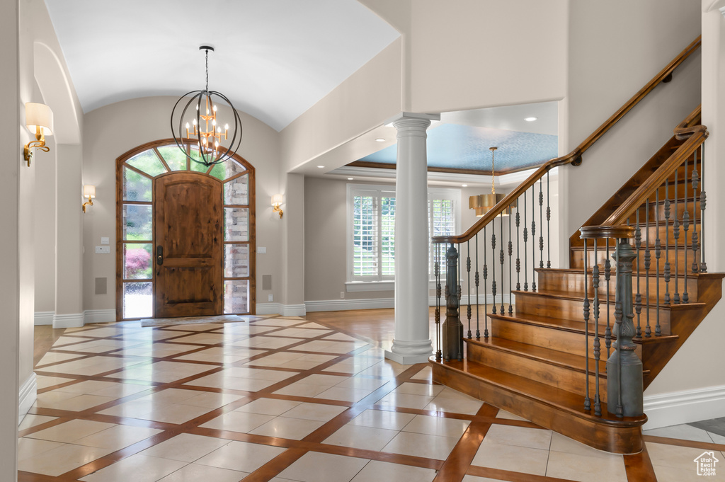 Foyer entrance featuring inlaid floor details, baseboards, ornate columns, a chandelier, and lofted ceiling