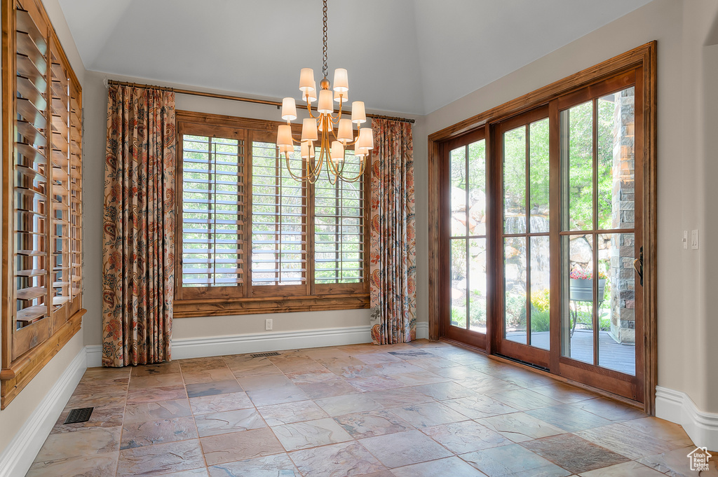 Unfurnished dining area with healthy amount of natural light, a chandelier, stone tile flooring, and lofted ceiling