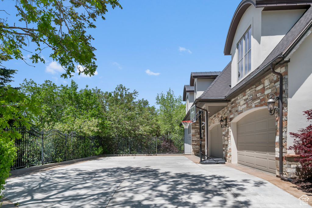 View of side of home with stone siding, stucco siding, fence, and a garage
