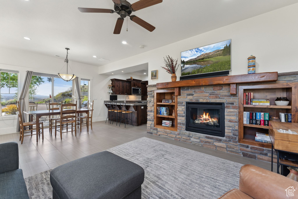 Living room with ceiling fan, a stone fireplace, baseboards, and recessed lighting