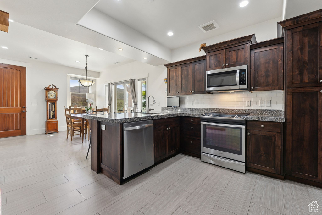 Kitchen featuring appliances with stainless steel finishes, tasteful backsplash, a sink, dark brown cabinetry, and a peninsula