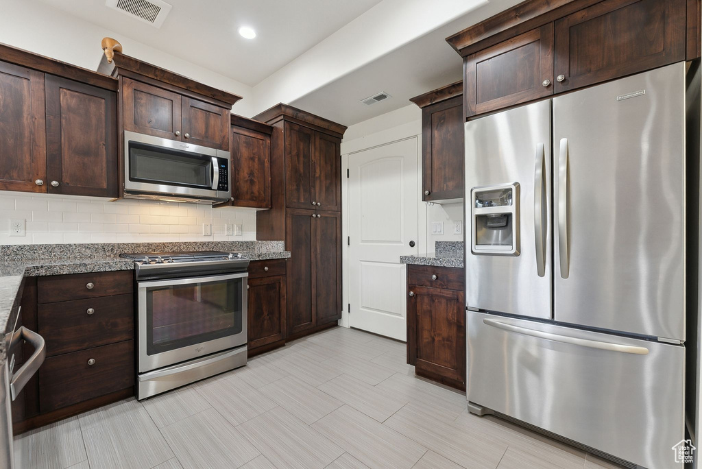 Kitchen featuring appliances with stainless steel finishes, tasteful backsplash, dark brown cabinets, dark stone countertops, and recessed lighting
