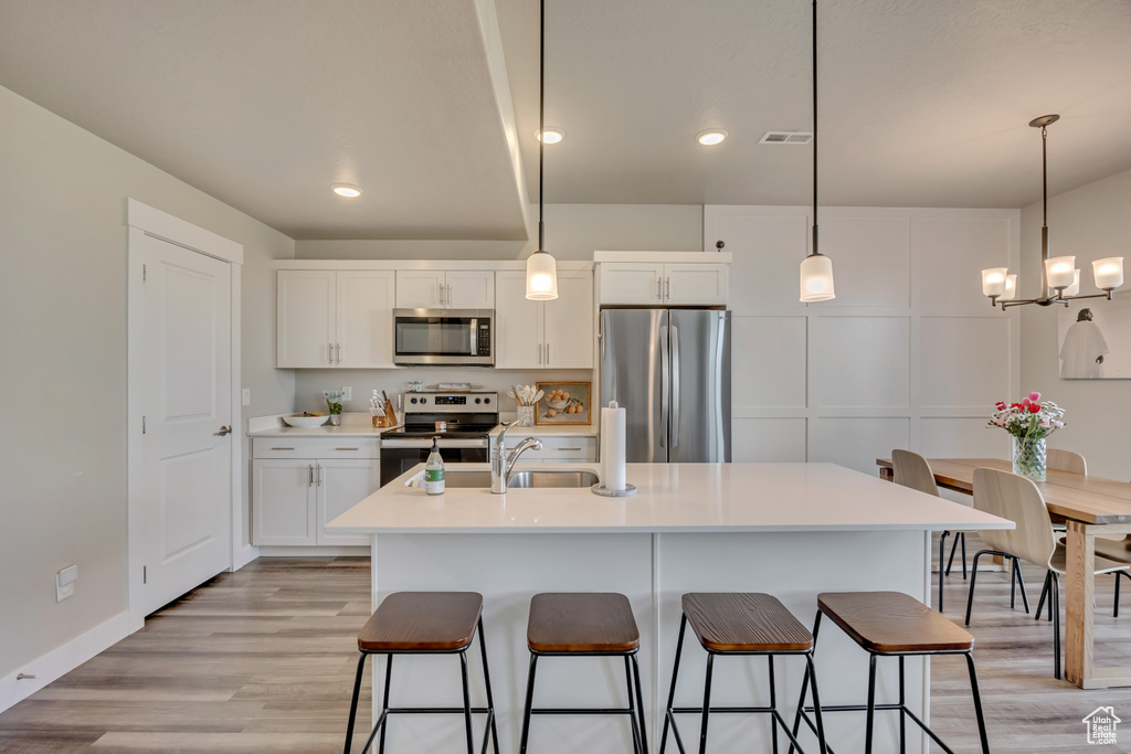 Kitchen with appliances with stainless steel finishes, a kitchen breakfast bar, white cabinets, light wood finished floors, and recessed lighting