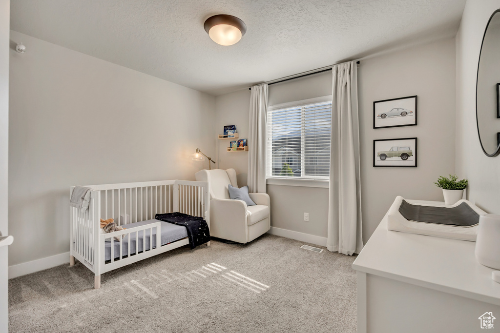 Bedroom featuring carpet floors, a nursery area, a textured ceiling, and baseboards