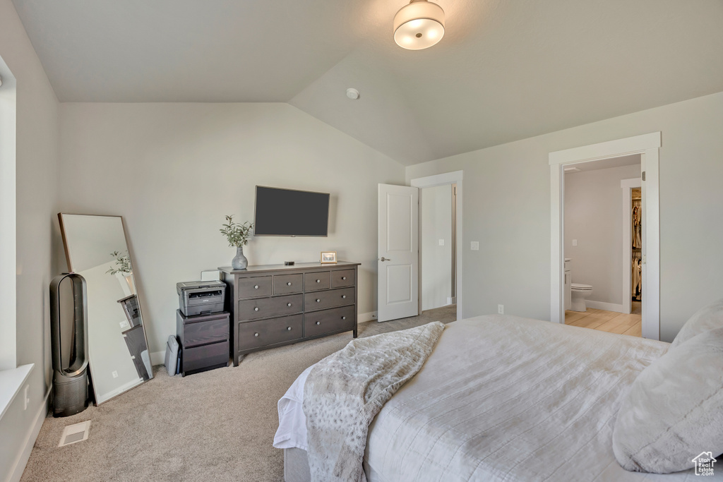 Bedroom with vaulted ceiling, ensuite bathroom, baseboards, and light colored carpet
