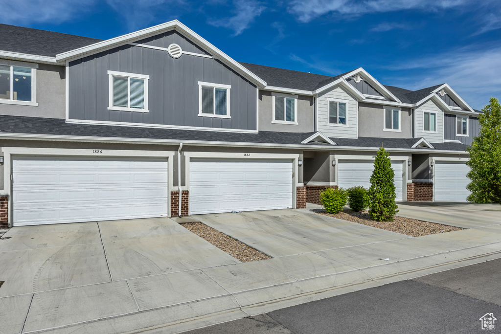 Townhome / multi-family property with brick siding, a garage, driveway, and roof with shingles