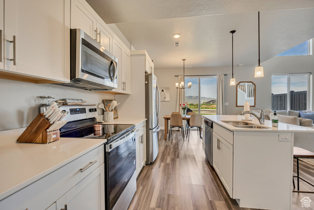 Kitchen with stainless steel appliances, a sink, a chandelier, wood finished floors, and white cabinetry