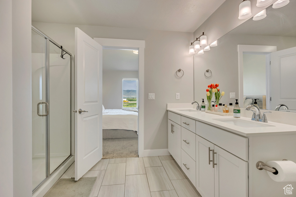 Ensuite bathroom featuring a shower stall, double vanity, and baseboards