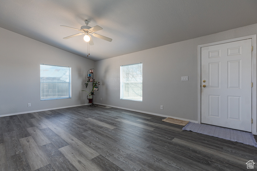 Empty room with a ceiling fan, dark wood finished floors, baseboards, and vaulted ceiling
