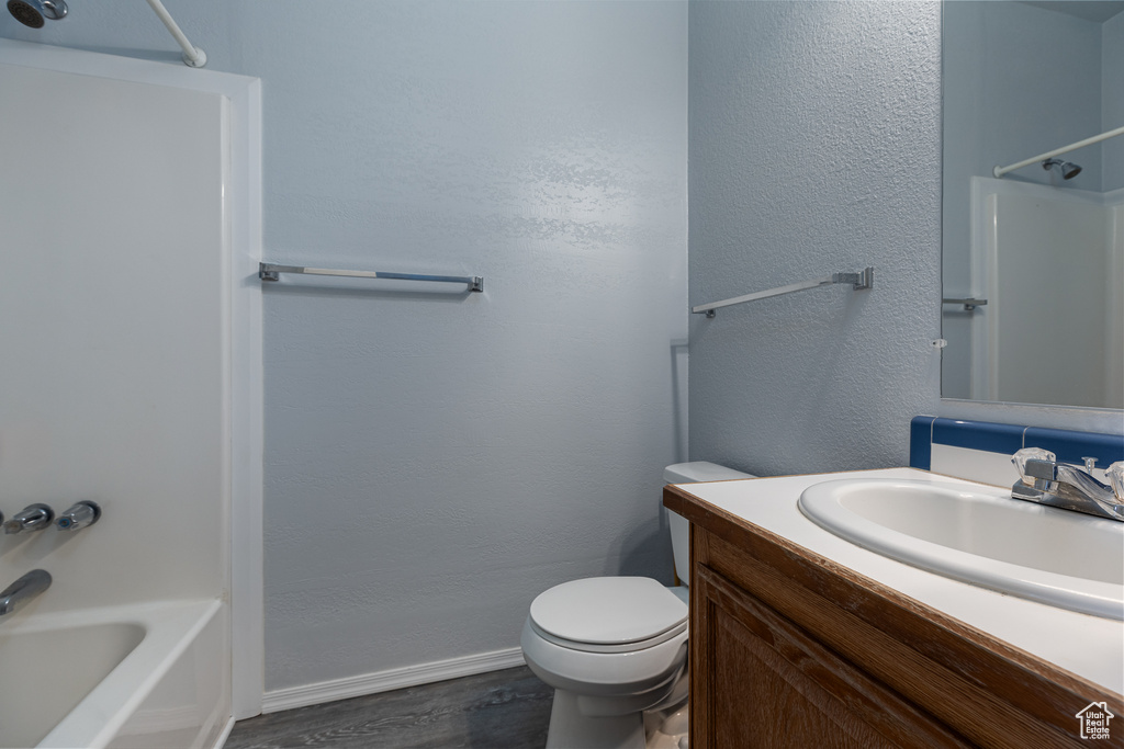Bathroom featuring baseboards, wood finished floors, toilet, vanity, and shower / tub combination