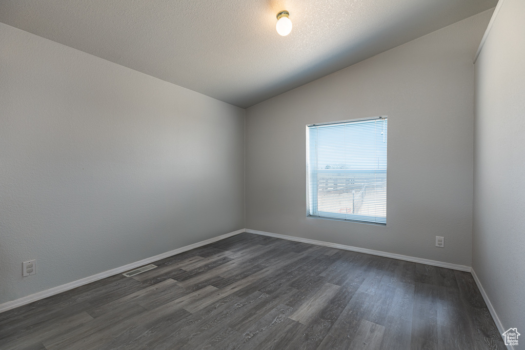 Empty room with lofted ceiling, dark wood-type flooring, and baseboards