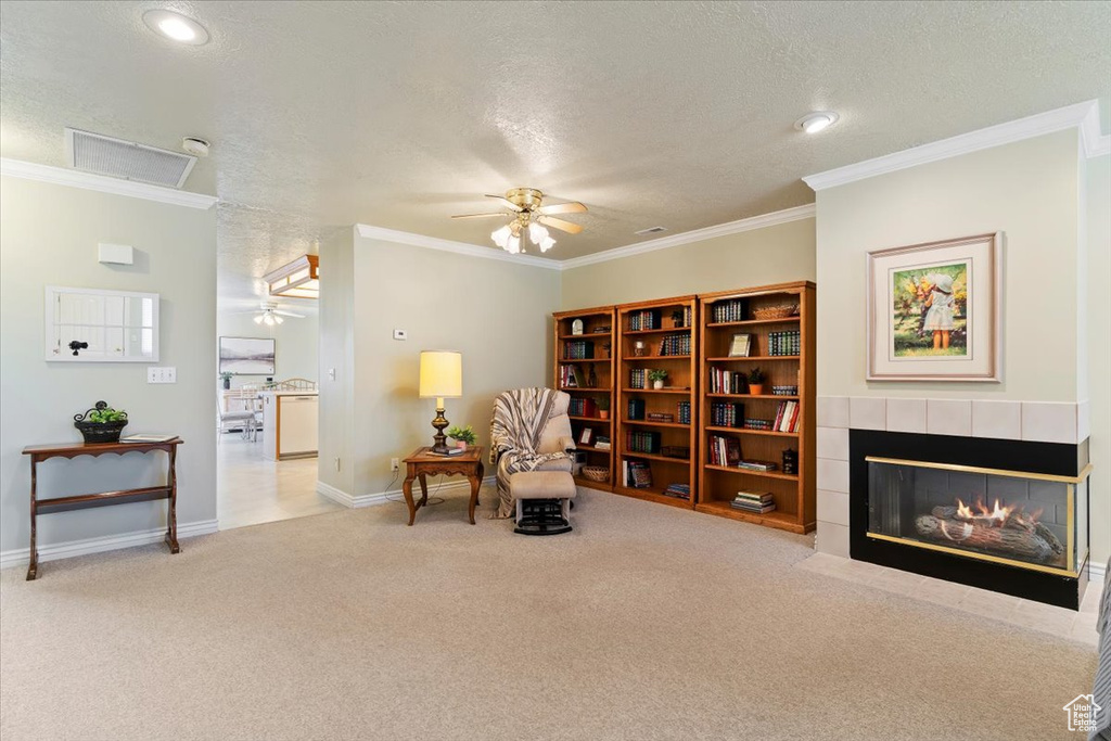 Living area featuring ceiling fan, a textured ceiling, carpet floors, a fireplace, and ornamental molding