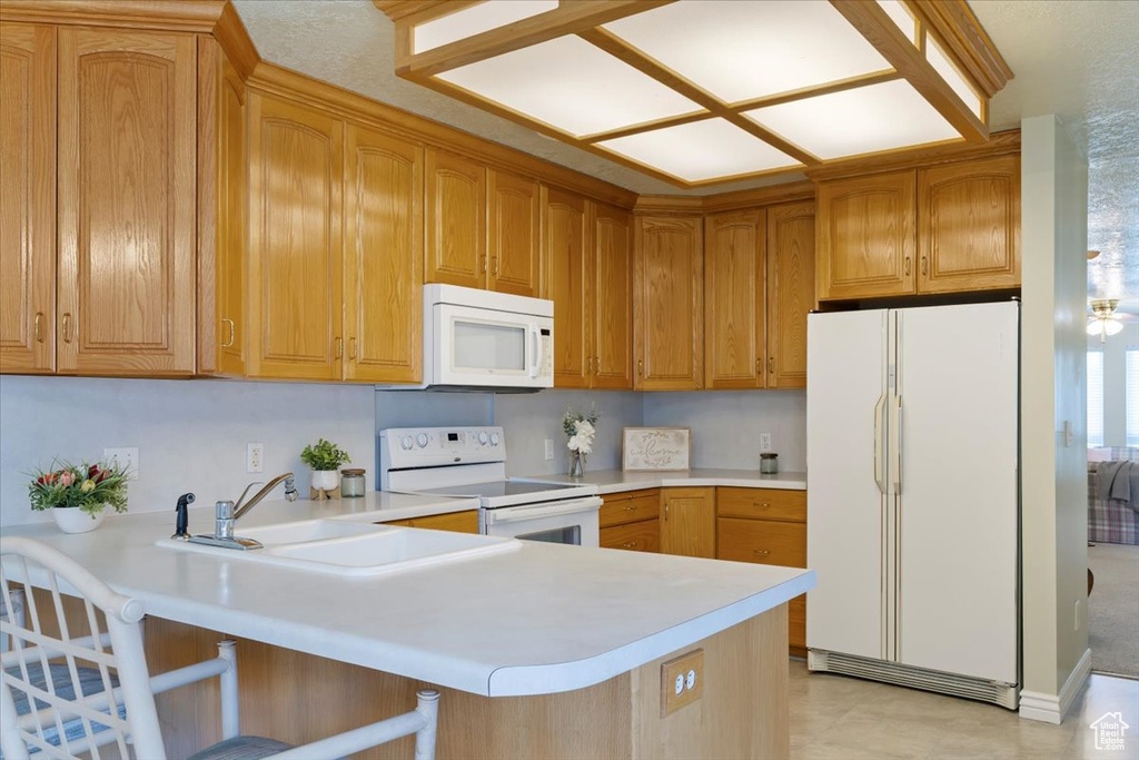 Kitchen featuring white appliances, a peninsula, light countertops, a kitchen breakfast bar, and a sink