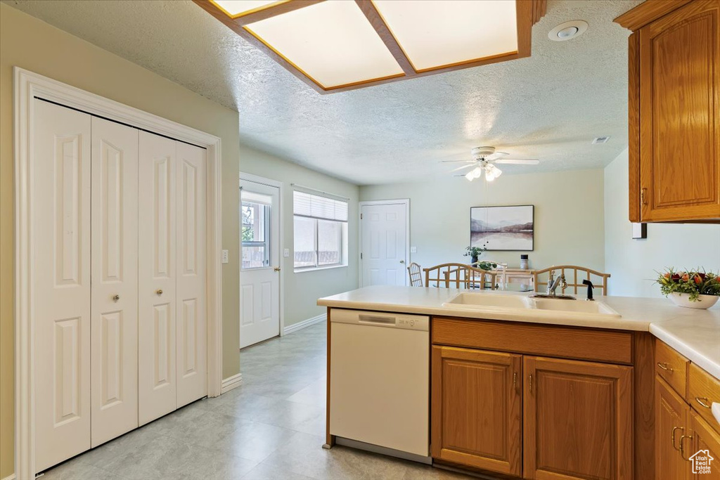 Kitchen featuring white dishwasher, a sink, a peninsula, brown cabinets, and a textured ceiling