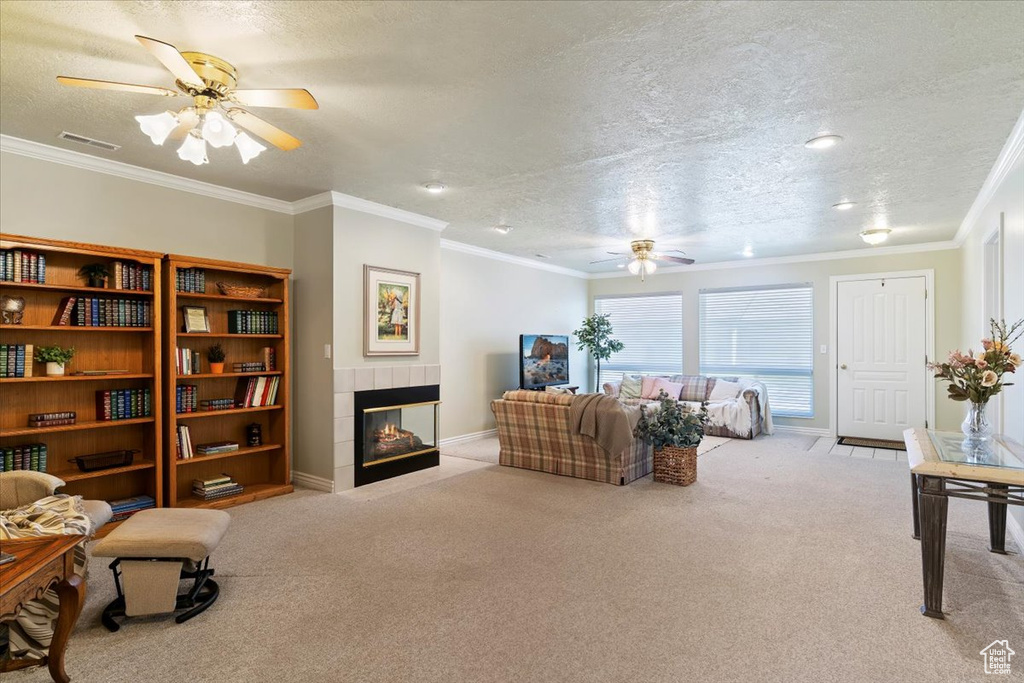 Carpeted living room with a ceiling fan, a fireplace, a textured ceiling, ornamental molding, and baseboards