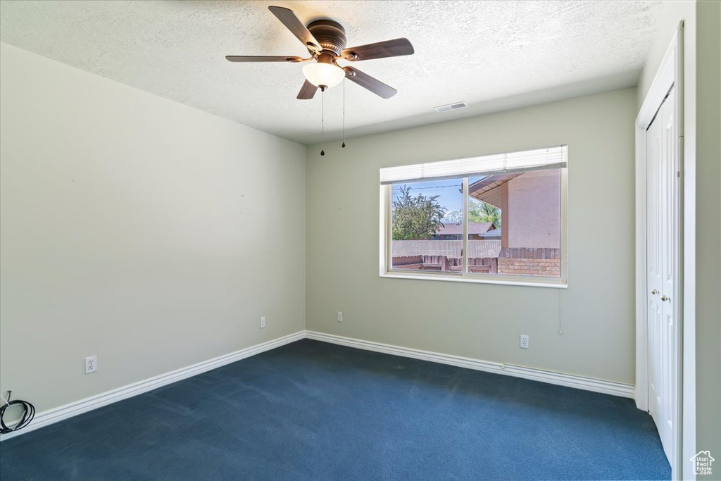 Spare room featuring ceiling fan, dark colored carpet, a textured ceiling, and baseboards