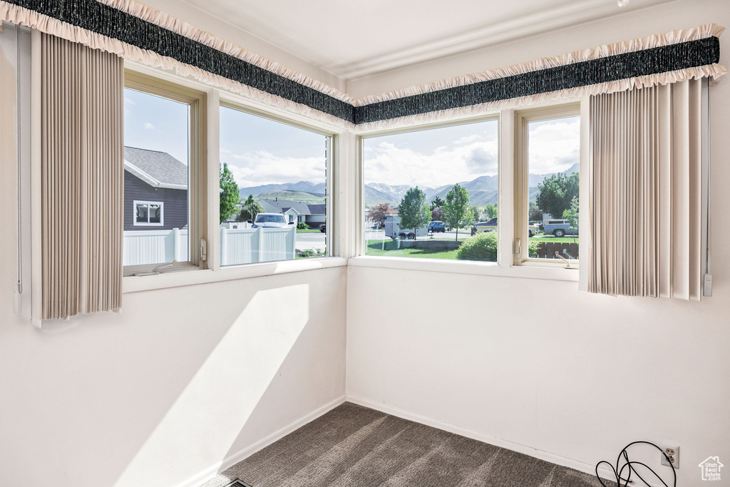 Spare room featuring healthy amount of natural light, a mountain view, dark colored carpet, and baseboards