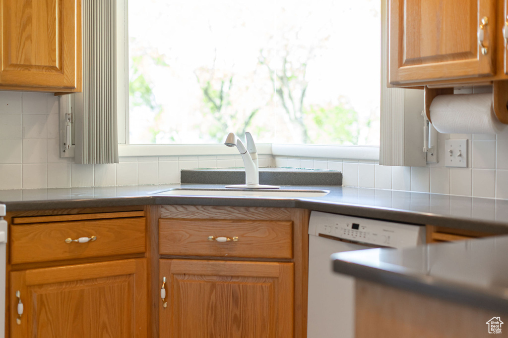Kitchen featuring dishwasher, a sink, backsplash, and brown cabinets