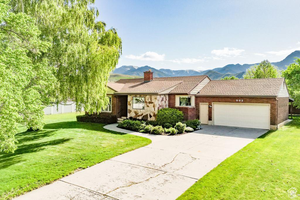 View of front of home featuring brick siding, a mountain view, an attached garage, and a front lawn