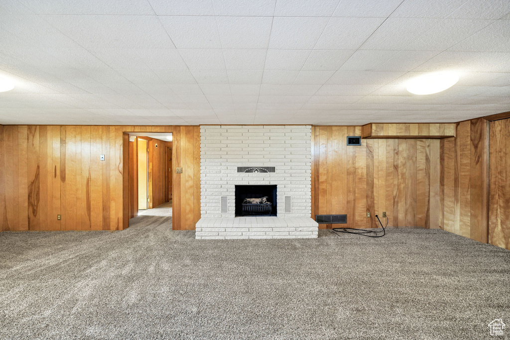 Unfurnished living room with carpet flooring, a fireplace, and wooden walls