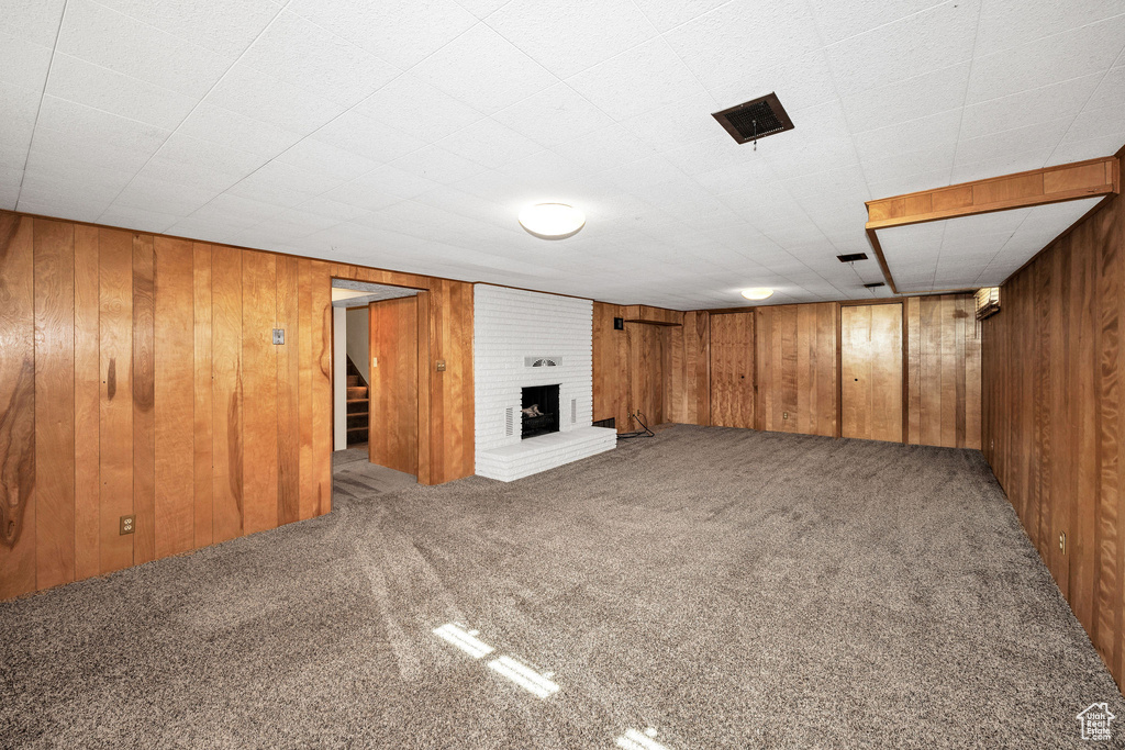 Finished basement featuring carpet floors, stairway, wooden walls, and a brick fireplace