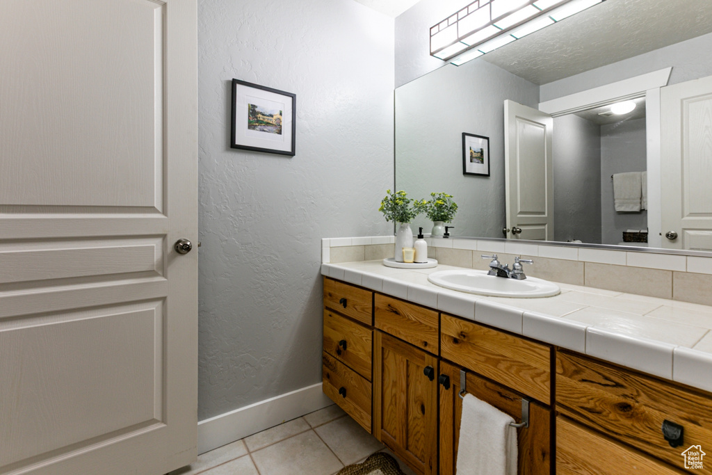 Bathroom featuring tile patterned floors, vanity, baseboards, and a textured wall