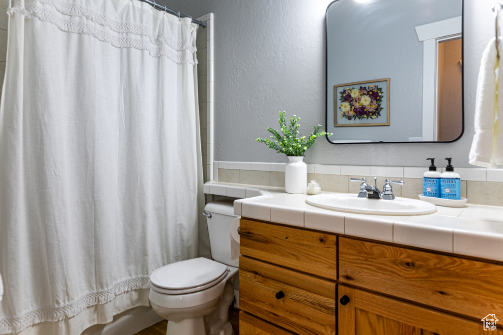 Bathroom with toilet, vanity, curtained shower, and a textured wall