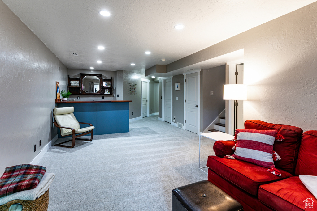 Living area with a textured wall, stairs, recessed lighting, light carpet, and baseboards