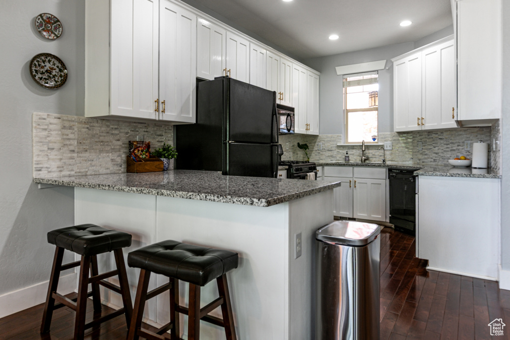 Kitchen with black appliances, a peninsula, dark wood-type flooring, recessed lighting, and white cabinets