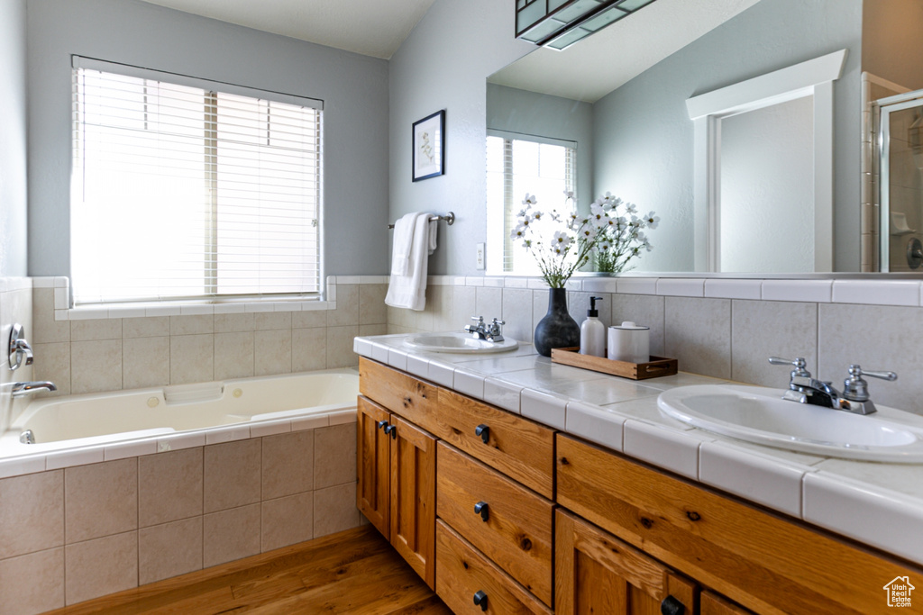 Full bath with wood finished floors, a shower stall, a bath, and double vanity
