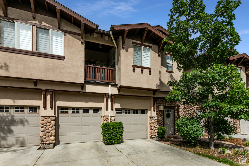 View of property with a balcony, a garage, driveway, and stucco siding