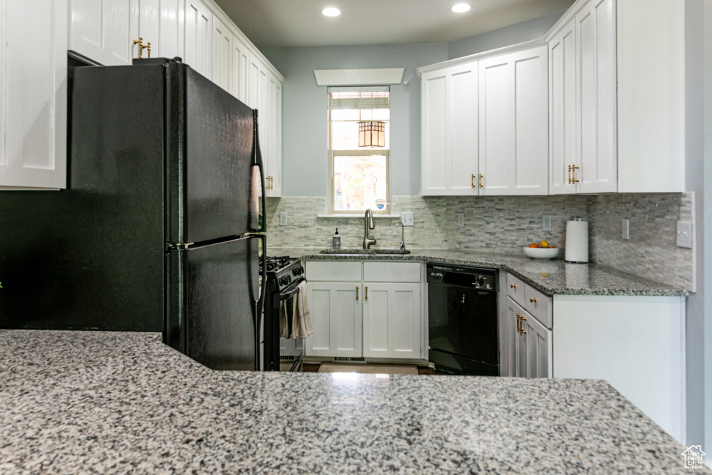 Kitchen with black appliances, a sink, backsplash, light stone countertops, and white cabinetry