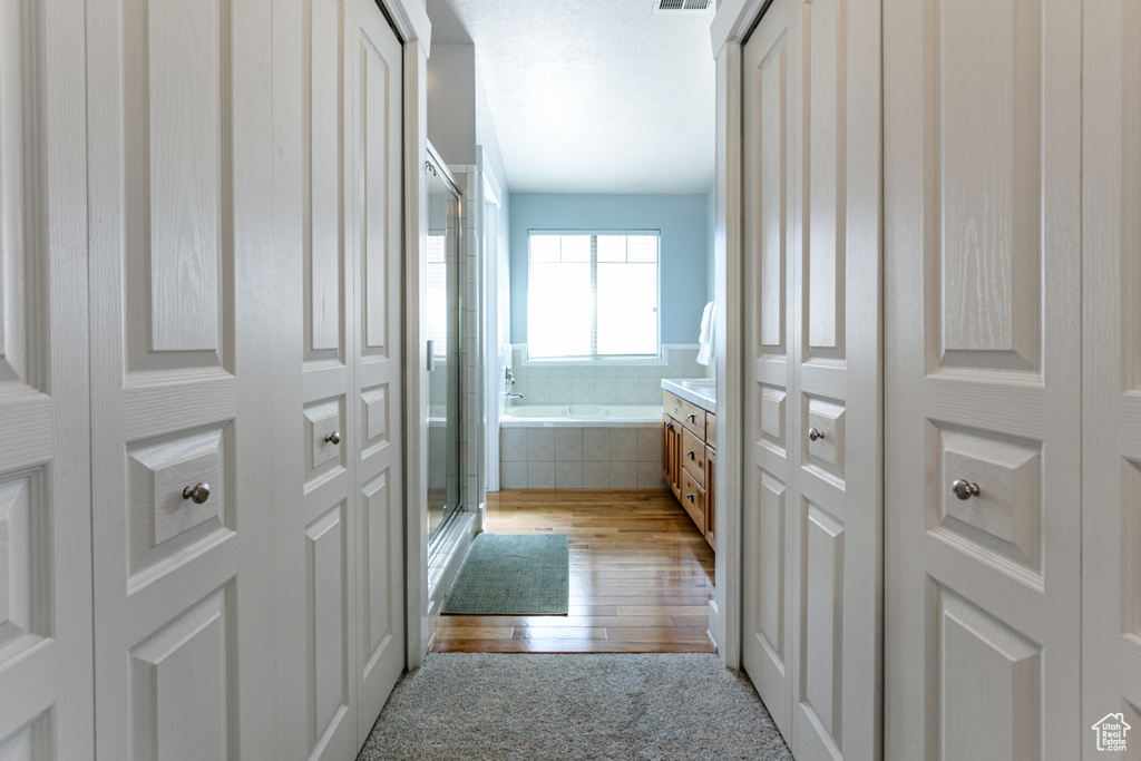 Full bath featuring a shower stall, a garden tub, wood-type flooring, and a closet