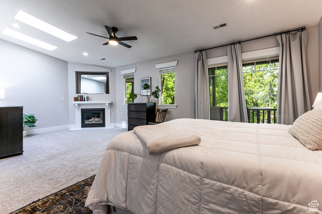 Bedroom with vaulted ceiling, a fireplace with flush hearth, baseboards, carpet, and a skylight