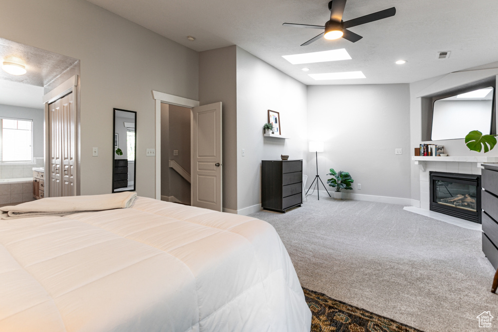 Bedroom with carpet, a glass covered fireplace, a skylight, baseboards, and ceiling fan