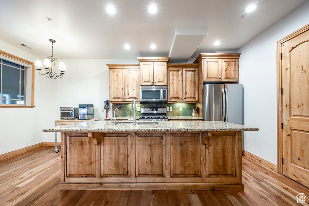 Kitchen featuring appliances with stainless steel finishes, baseboards, wood finished floors, a kitchen island with sink, and recessed lighting